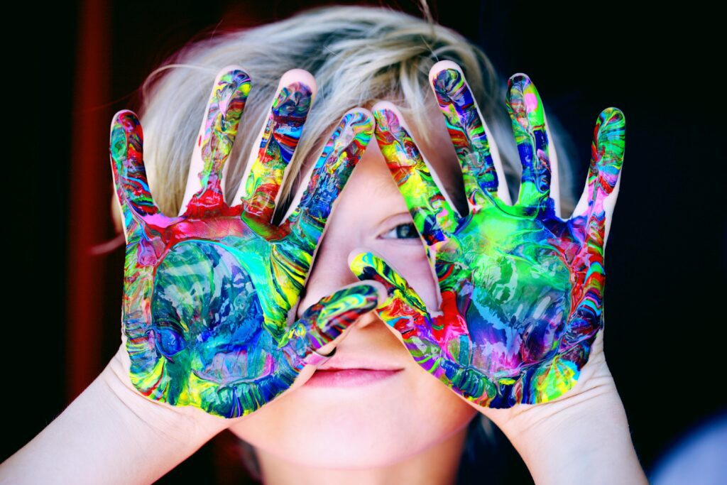 Vibrant close-up of a child's hands covered in alt="child expressing creativity through painting in a reforming education setting" colorful paint, expressing creativity and fun.