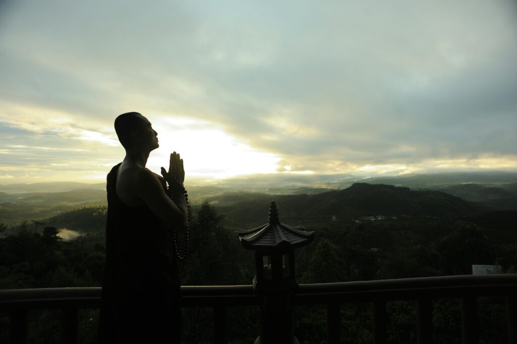 Islamic view of human creativity and purpose A monk in silhouette prays peacefully at sunrise with mountains in the background.