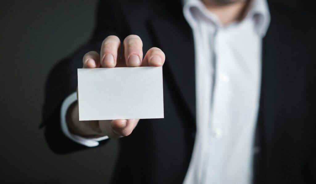 modern business card template in Canva for beginners" A man in a suit presenting a blank business card for corporate usage.