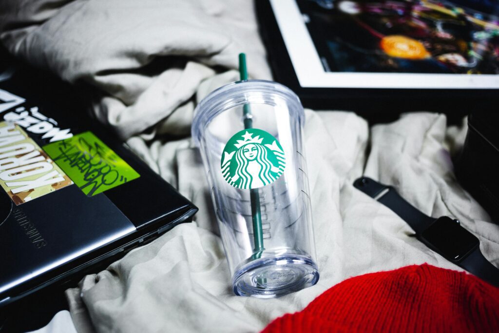 A clear Starbucks cup with straw on a casual bed setup.