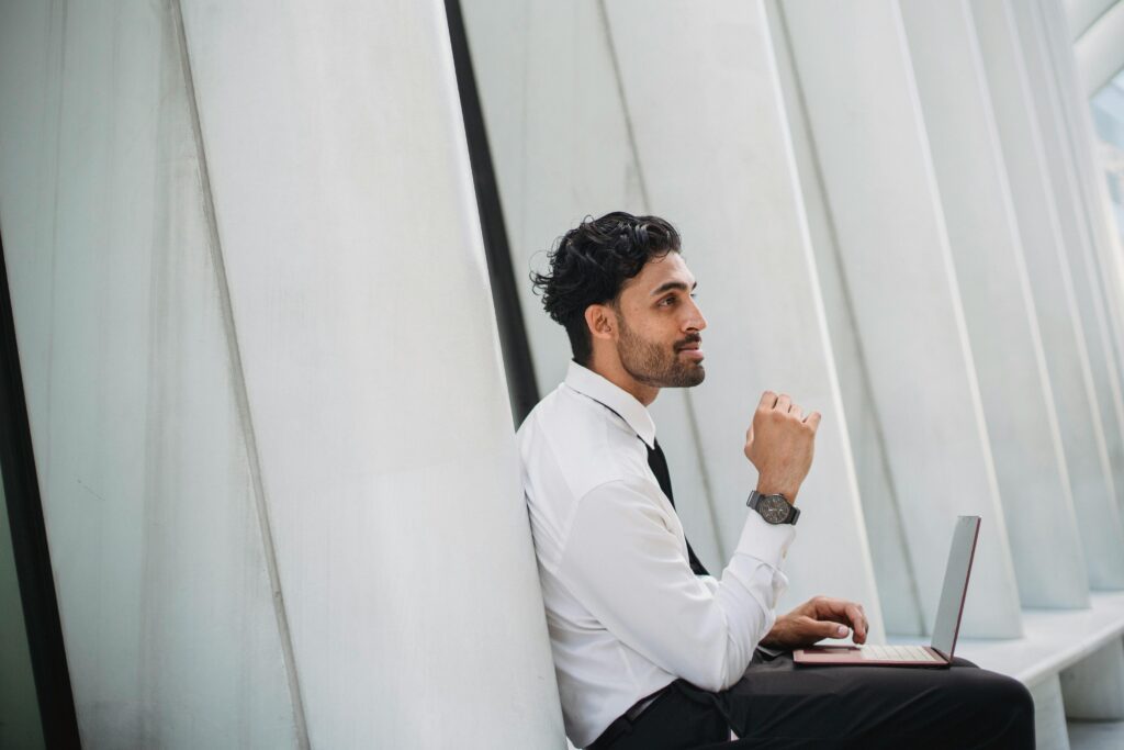 Bearded man in corporate attire using a laptop indoors with modern architecture.