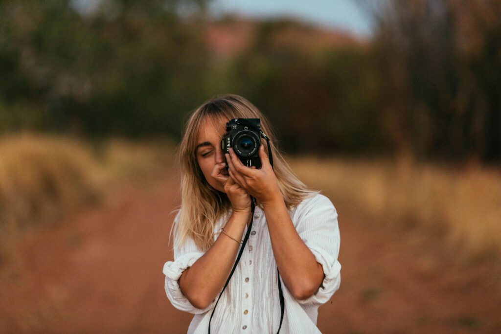 Female photographer in white shirt taking photos in natural outdoor setting.
