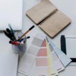 Organized workspace featuring color swatches, notebook, laptop, and stationery for design projects.