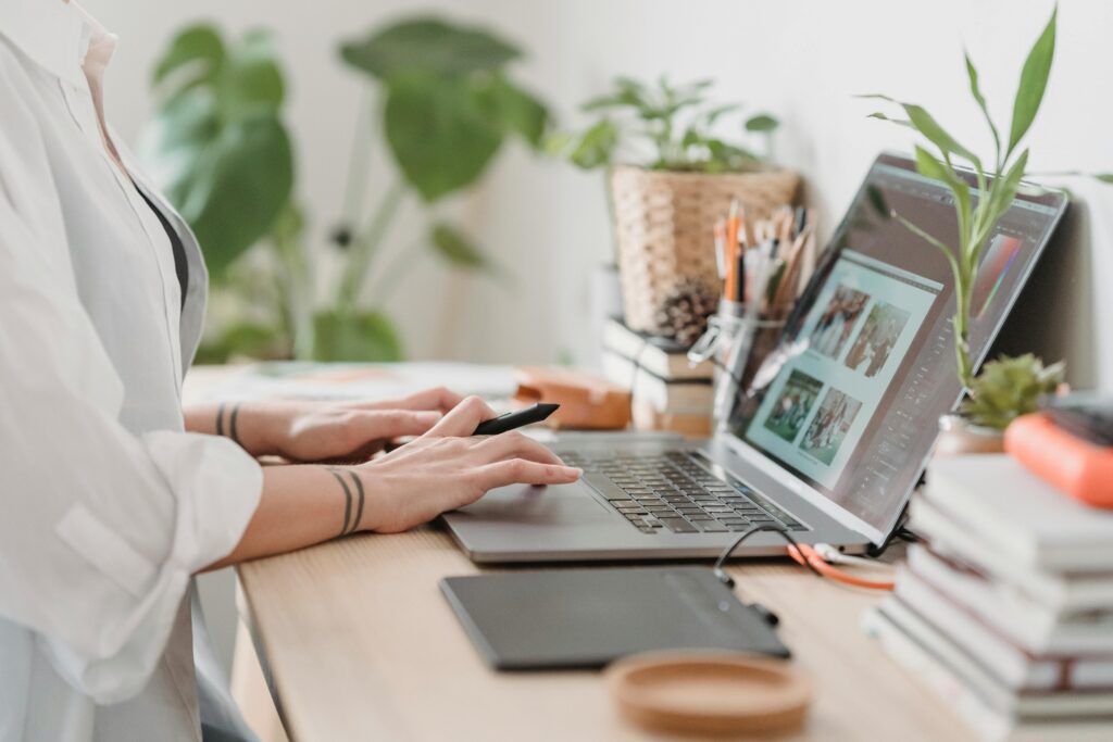 pexels photo 7014337 7014337 Freelance designer working from home using a laptop and digital tablet, surrounded by plants.